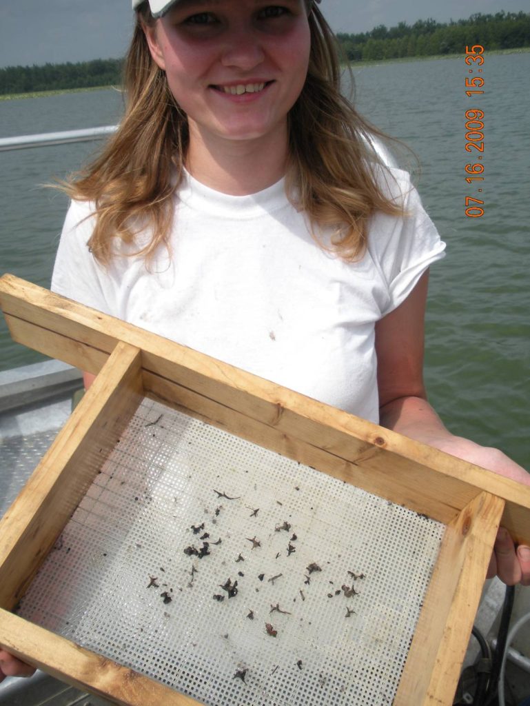 A young woman holds up a seive.